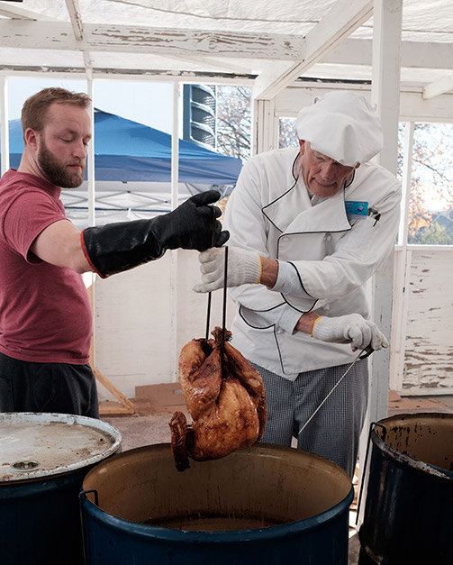 man pulling fried turkey out of vat of vegetable oil